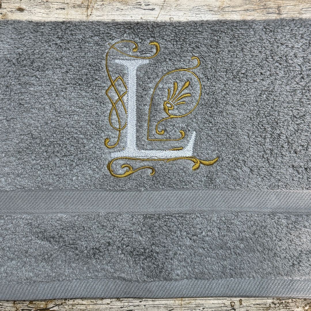 Gray towel with gold embroidered letter 'L' on a wooden surface