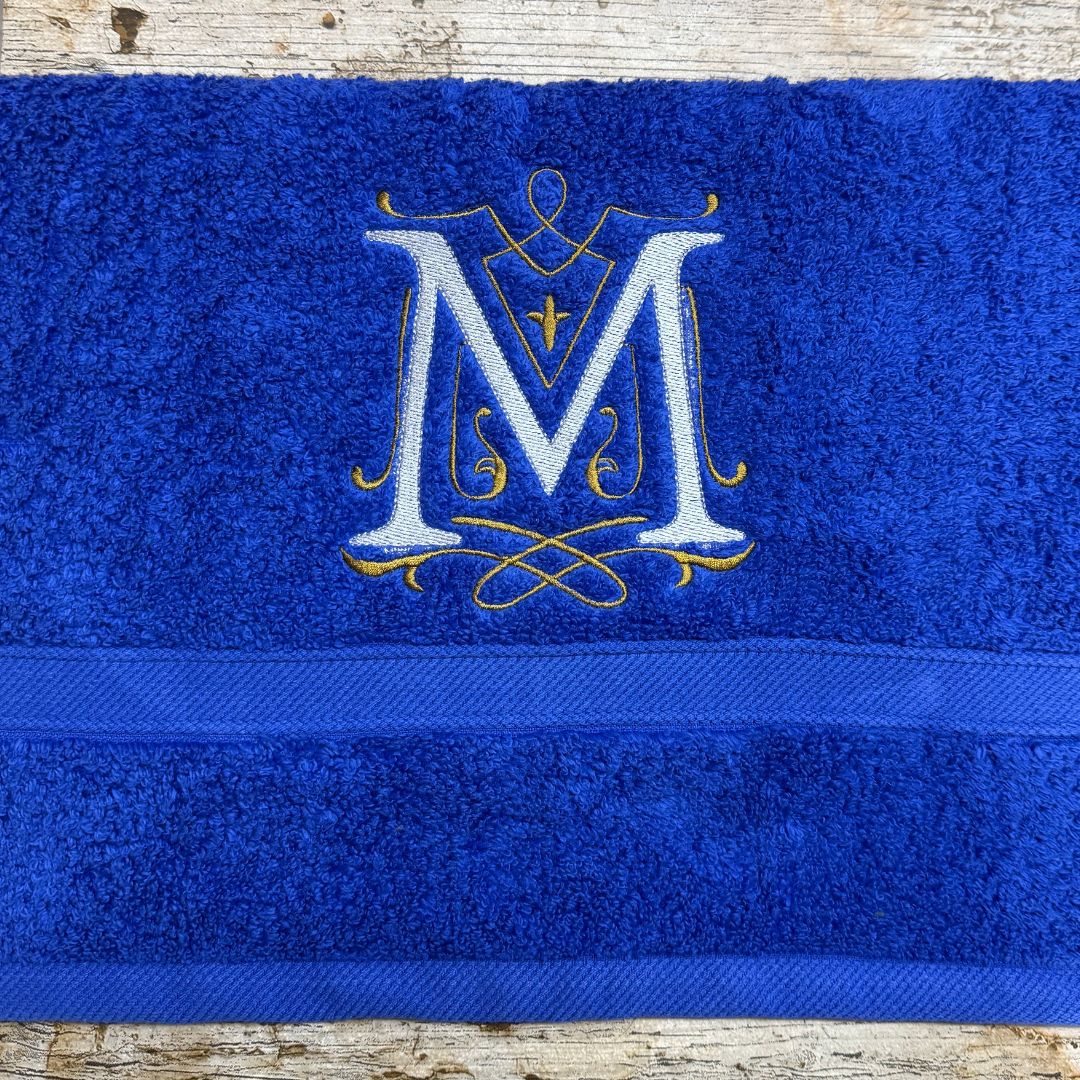 Blue towel with gold embroidered letter 'M' on a wooden surface