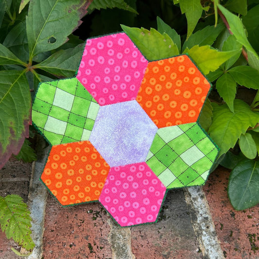 Colorful hexagonal patchwork design on a brick surface with green leaves in the background
