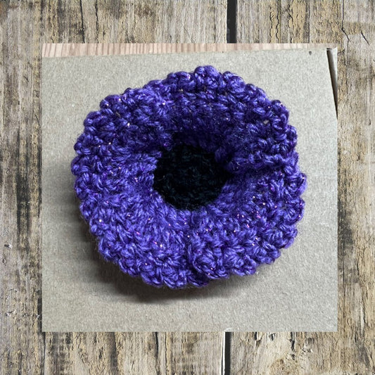Purple crocheted flower on a gray card with a wooden background