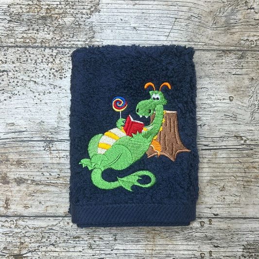 Navy blue towel with a green dragon reading a book design on a wooden surface