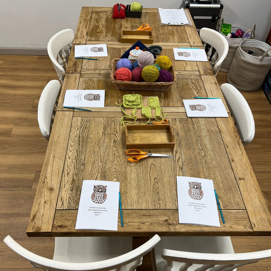 Wooden dining table with yarn, knitting needles, and other crafting supplies on a wooden floor.
