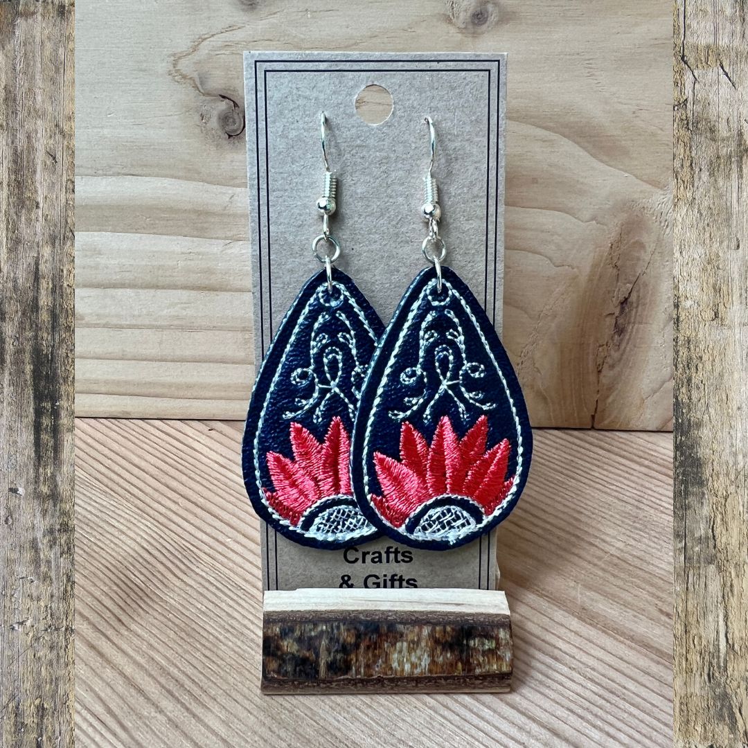 A pair of embroidered teardrop-shaped dangle earrings displayed on a gray card stand. The earrings have a dark navy blue background with white embroidered floral patterns and a red lotus flower motif at the bottom, hanging from silver fishhook wires.