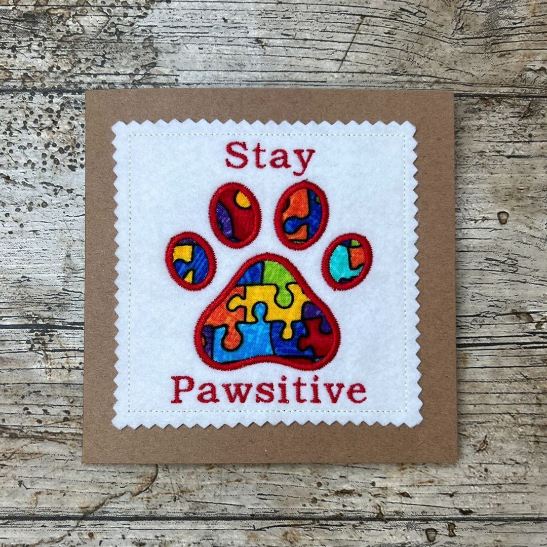 Patch with colorful paw print and text 'Stay Pawsitive' on a wooden surface