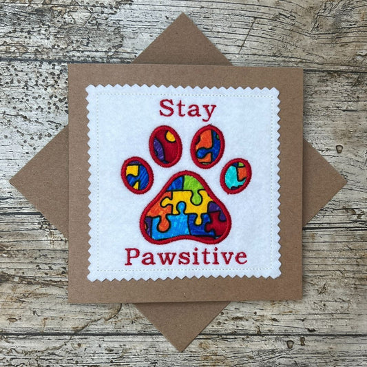 Card with colorful paw print and text 'Stay Pawsitive' on a wooden surface