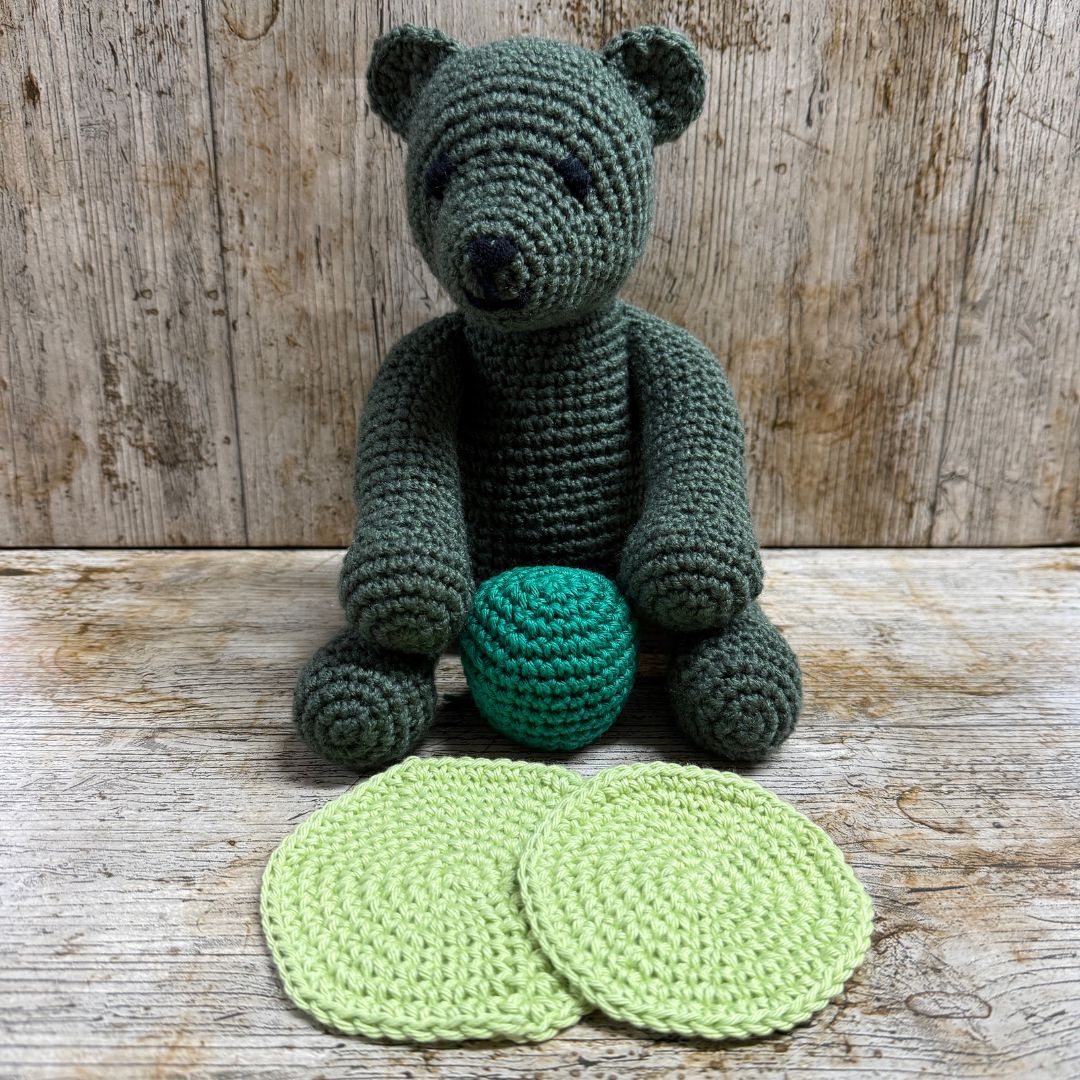 Crocheted bear toy with a teal ball on a wooden surface