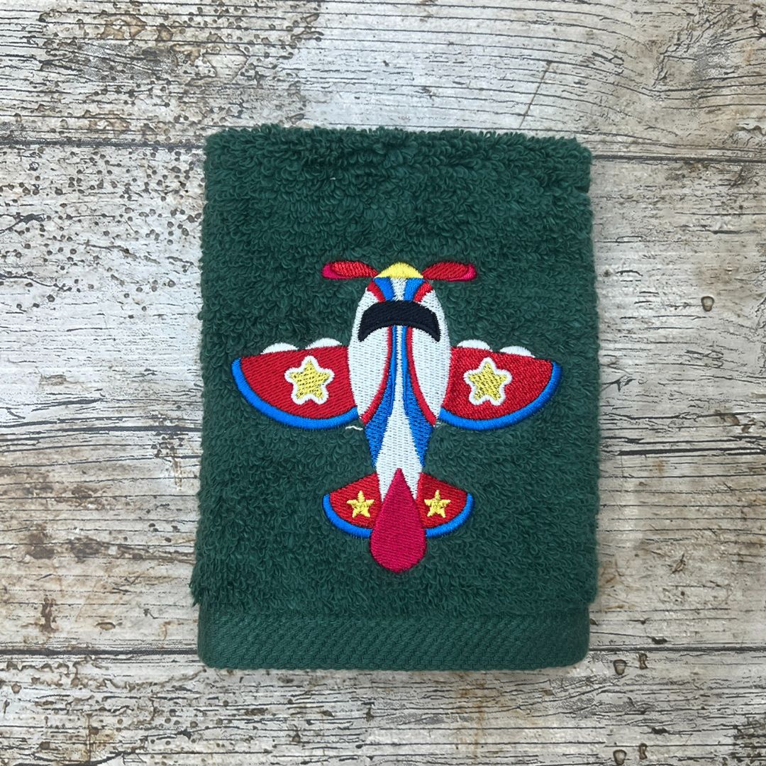 Beautiful Toy Plane design, embroidered onto a green face cloth and placed on a wooden background, by Coralie's Crafts & Gifts.