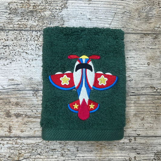 Beautiful Toy Plane design, embroidered onto a green face cloth and placed on a wooden background, by Coralie's Crafts & Gifts.