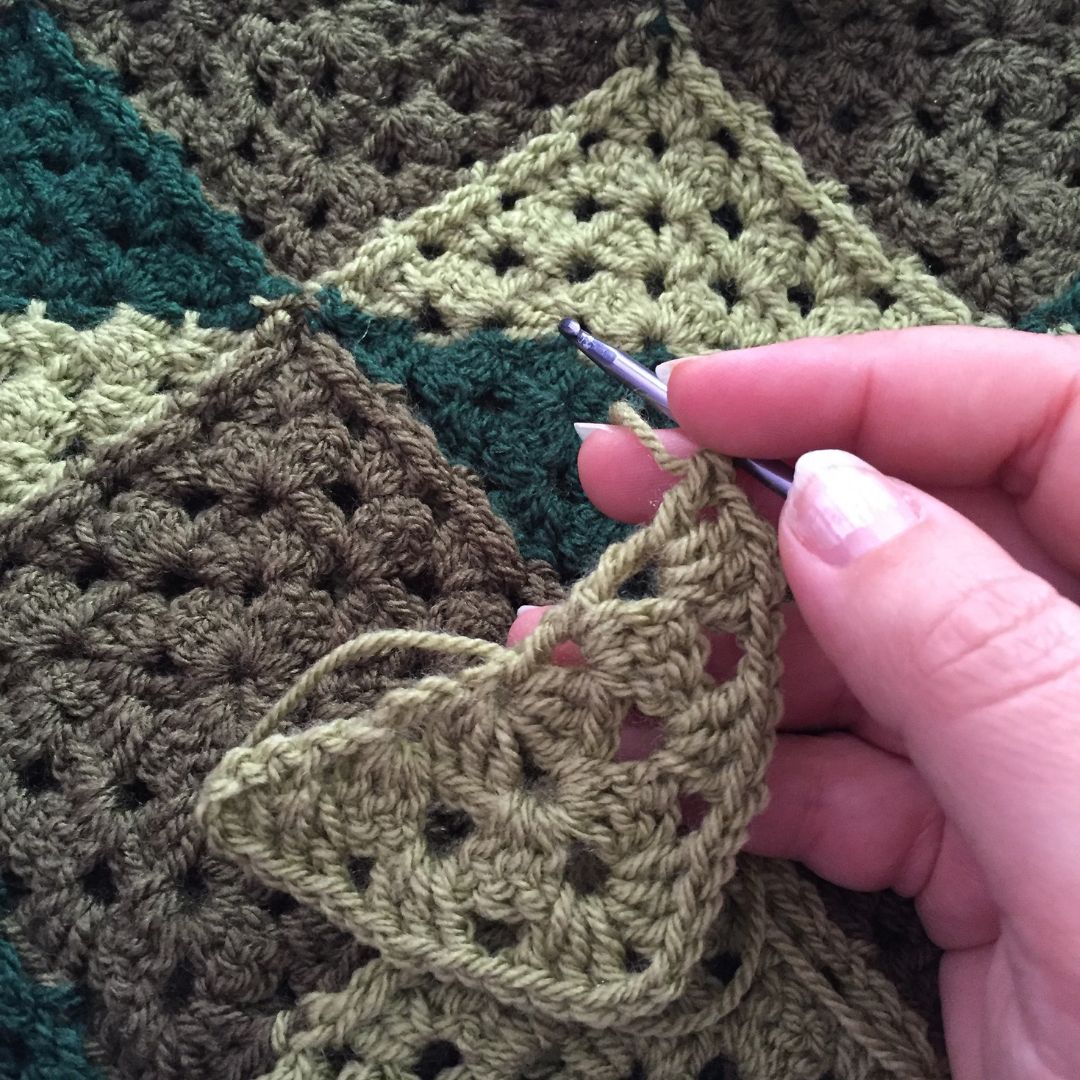 Hand crocheting a green fabric with a pattern, using a crochet hook.