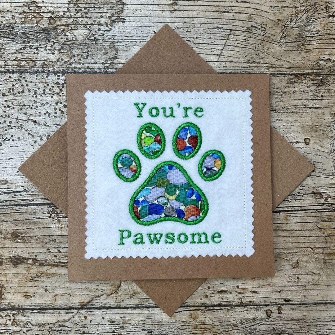 Card with colorful paw print and 'You're Pawsome' text on a wooden surface