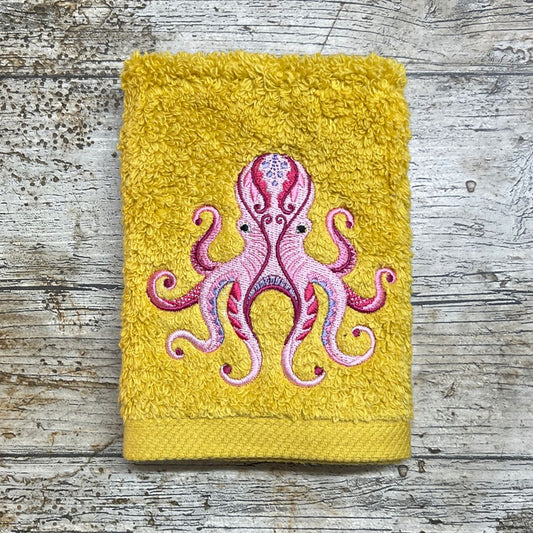 Funky Octopus on a Yellow face cloth on a wooden background. The octopus is embroidered onto the face cloth
