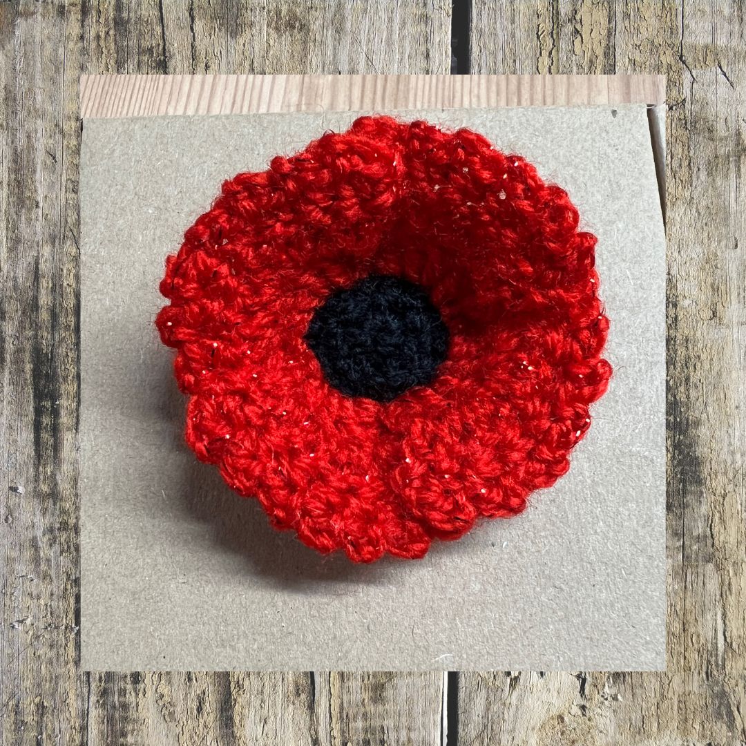 Red crocheted poppy flower on a gray card with a wooden background
