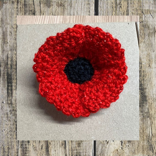 Red crocheted poppy flower on a gray card with a wooden background